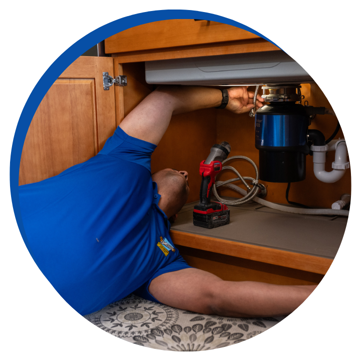 Technician in a blue uniform using equipment to clean a drain in a bathroom.